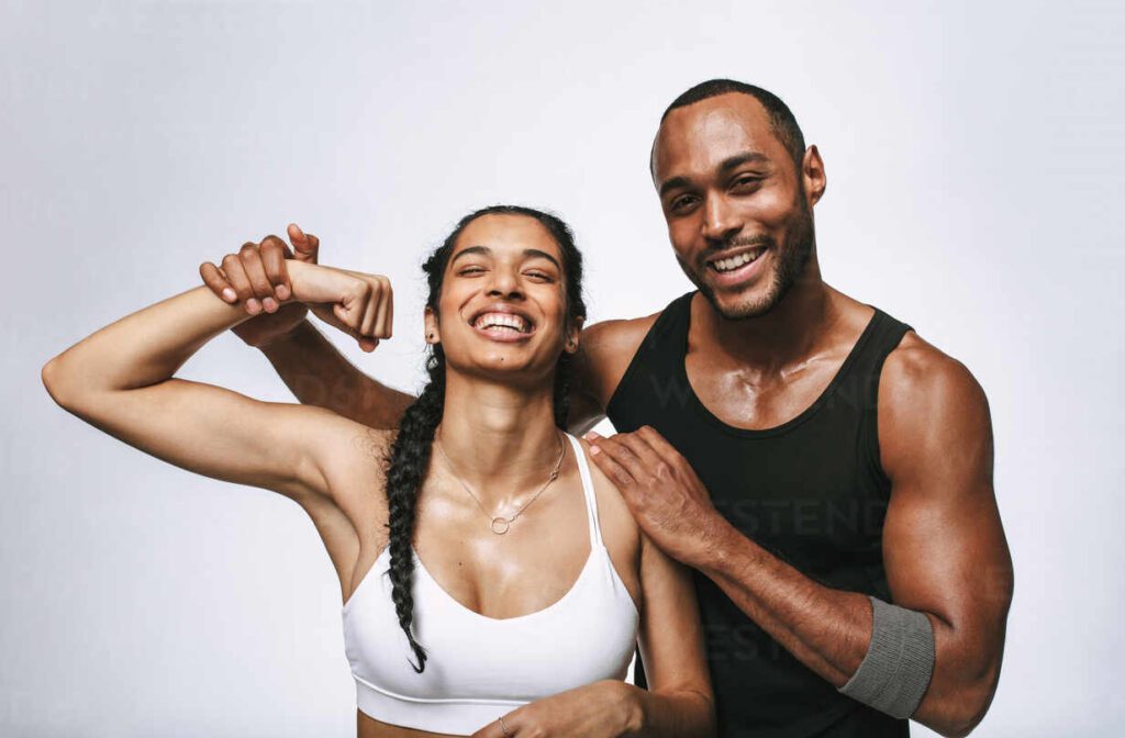 Couple smiling at the gym after a workout, woman flexing biceps with training partner